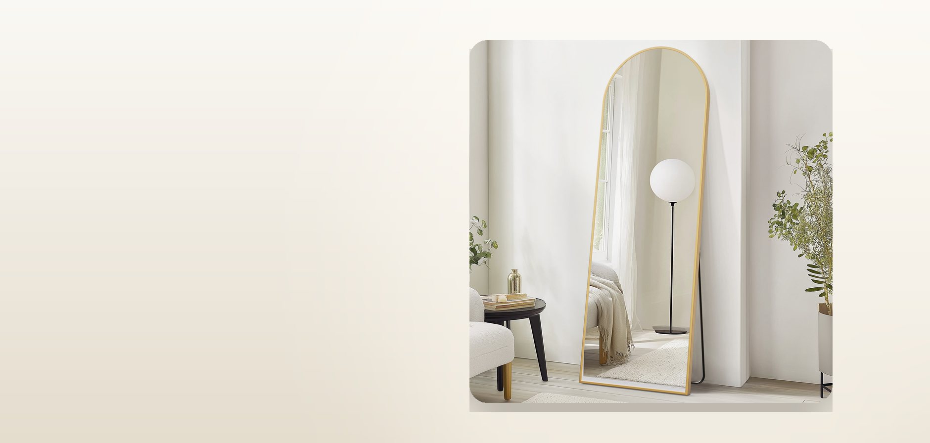 An arched full-length floor mirror with a gold metal frame, leaning against a wall in a bright room.